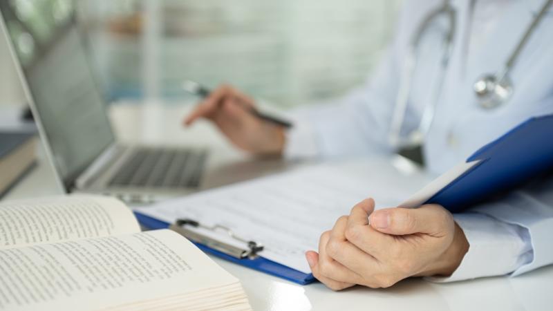 Doctor with computer, clipboard and a book open